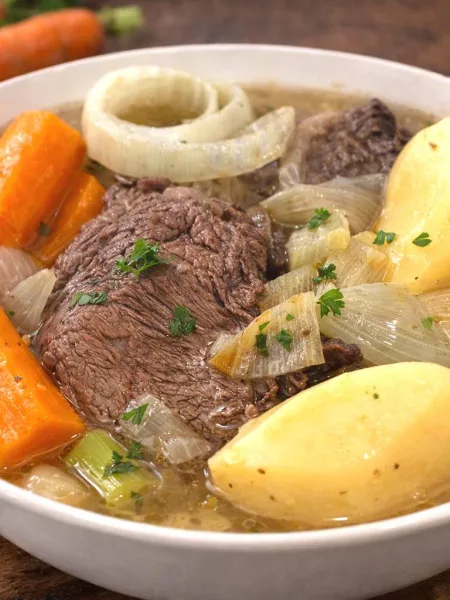 Pot-au-feu traditionnel avec carottes, boeuf, oignon, dans une assiette creuse blanche.