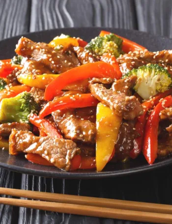 Wok de boeuf aux légumes croquants dans une assiette noire, avec une paire de baguettes à côté.