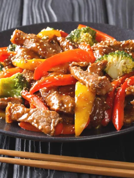 Wok de boeuf aux légumes croquants dans une assiette noire, avec une paire de baguettes à côté.