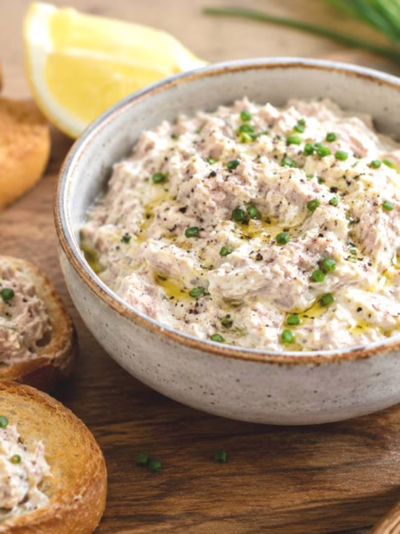 Rillettes de thon au fromage frais dans un saladier blanc avec deux tartines garnies à côté.